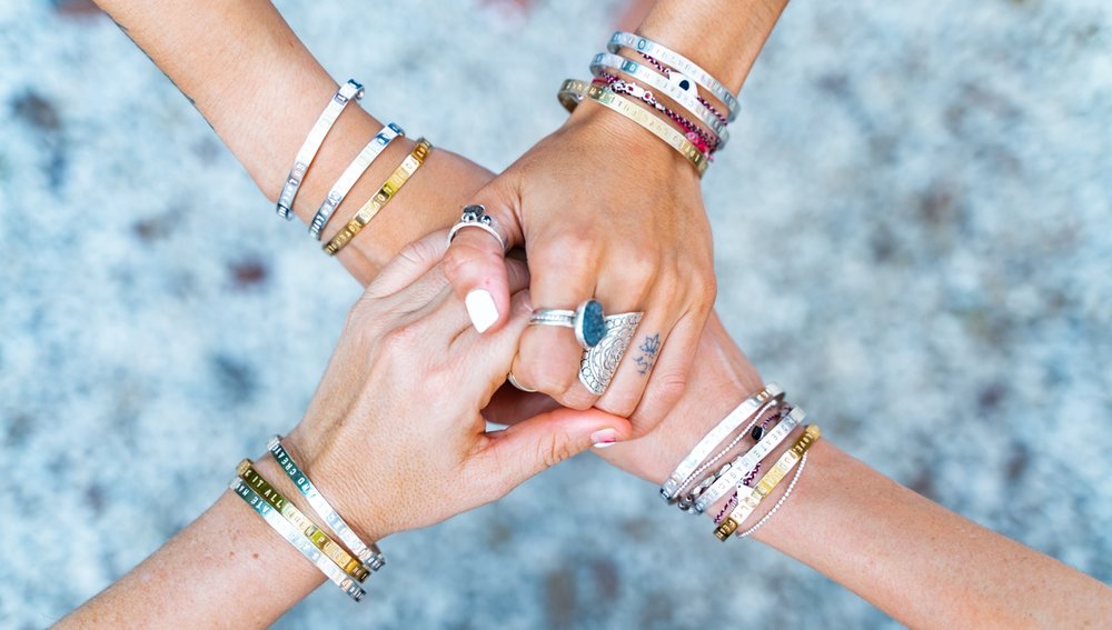 Four women holding hands and wearing Water Thru Skin Bracelets on their wrists